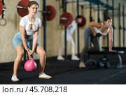 Young girl doing exercises with kettlebell near other people in crossfit gym. Стоковое фото, фотограф Яков Филимонов / Фотобанк Лори