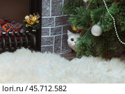 A white British cat with yellow eyes peeks out from under a Christmas tree near the fireplace. Стоковое фото, фотограф Неведицына Елена / Фотобанк Лори