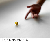 Hand rolling yellow dice on white surface representing chance and risk in game. Стоковое фото, фотограф Lamina Akulova / Фотобанк Лори