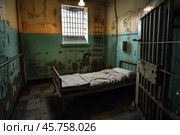 Empty prison cell bed in deteriorated room with barred window. Стоковое AI-изображение, AI-художник Иван Рябоконь / Фотобанк Лори