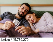 Пара лёжа в постели держит блистер презерватива. Стоковое AI-изображение, AI-художник Anna Leeva / Фотобанк Лори