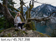 Girl sits on a tree and meditates on blue lake background. Lake Ritsa in Abkhazia. Стоковое фото, фотограф Степанов Григорий / Фотобанк Лори