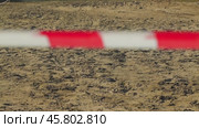 The sandy area is fenced with a red-and-white striped ribbon. The uneven terrain is a construction or restricted area. The tape is in the foreground, blurred. Стоковое видео, видеограф Воловодов Владимир / Фотобанк Лори