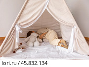 Happy little caucasian boy is lying in a wigwam. Childhood, playing with soft toys, tenderness. Children's room with a teepee tent. Cozy atmosphere interior of a children's room. Стоковое фото, фотограф Ирина Михайличенко / Фотобанк Лори