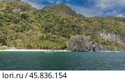 A beautiful beach on a tropical island. Rows of palm trees on the sandy coast. Tiny silhouettes of people, boats in the ocean. Picturesque cliffs by the water. Mountains with green vegetation. Стоковое фото, фотограф Вера Ивановна Кубарева / Фотобанк Лори