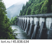 Dam with Waterfall on the River. Hydroelectric dam during Spring runoff, full water. Water rushing out of opened gates of hydro electric power dam. Concrete foothill and wall. Renewable energy systems. Стоковое AI-изображение, AI-художник Марина Демидюк / Фотобанк Лори