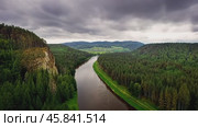 River flows through green forest near rocky cliff under cloudy sky. Стоковое AI-видео, аниматор Юрий Поздников / Фотобанк Лори