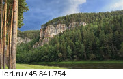 Majestic river flows near pine forest and rocky cliff under cloudy sky. Стоковое AI-видео, аниматор Юрий Поздников / Фотобанк Лори