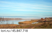 Autumn morning on the Kama River. A dirt road runs along the shoreline. There are thickets of reeds in the water. In the distance behind a small island with trees disperse remnants of fog. Стоковое фото, фотограф Роман Дзюбало / Фотобанк Лори