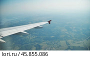 Airplane wing hovering over verdant countryside, revealing patchwork fields, rustic villages, and serpentine roads during sunny aerial journey. Стоковое видео, видеограф Mikhail Davidovich / Фотобанк Лори