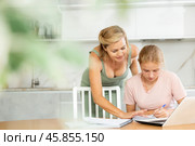 Mother looks at laptop and prompts and helps teen girl to write in notebook to complete task. Стоковое фото, фотограф Яков Филимонов / Фотобанк Лори
