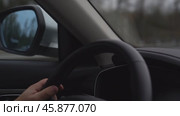 Person is driving a car and is holding the steering wheel. The car is on a road and there is a mirror on the side of the car. Стоковое видео, видеограф Скрипачев Антон / Фотобанк Лори