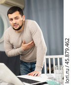 Guy suffering from chest pain standing near table with laptop at home. Стоковое фото, фотограф Яков Филимонов / Фотобанк Лори