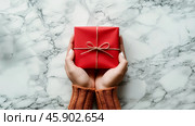 Hands gently hold a vibrant red gift adorned with a simple bow, symbolizing festive moments filled with joy, love, and anticipation for birthdays, New Year, and Valentine Day. Copy space. Стоковое AI-изображение, AI-художник Юлия Ильина / Фотобанк Лори
