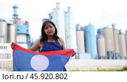 Sad young woman holding big flag of Laos against background of factory. Стоковое видео, видеограф Яков Филимонов / Фотобанк Лори