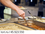 The hand of an unrecognizable volunteer puts nutritious food on a plate in a modern charity canteen. Стоковое фото, фотограф Darya Komarova / Фотобанк Лори