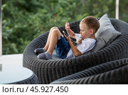 A 5-year-old little boy with a smartphone in his hands on the veranda. The child is playing on the phone. Harm of gadgets for children. Protect your child from the smartphone. Kids and gadgets. Стоковое фото, фотограф Photojuli / Фотобанк Лори