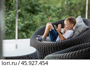 A 5-year-old little boy with a smartphone in his hands on the veranda. The child is playing on the phone. Harm of gadgets for children. Protect your child from the smartphone. Kids and gadgets. Стоковое фото, фотограф Photojuli / Фотобанк Лори