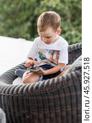 A 5-year-old little boy with a smartphone in his hands on the veranda. The child is playing on the phone. Harm of gadgets for children. Protect your child from the smartphone. Kids and gadgets. Стоковое фото, фотограф Photojuli / Фотобанк Лори