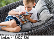 A 5-year-old little boy with a smartphone in his hands on the veranda. The child is playing on the phone. Harm of gadgets for children. Protect your child from the smartphone. Kids and gadgets. Стоковое фото, фотограф Photojuli / Фотобанк Лори