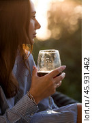 A glass of red alcoholic drink or wine in a woman's hand. A woman is resting on the veranda of a country house. The concept of relaxation, party or celebration. Стоковое фото, фотограф Photojuli / Фотобанк Лори