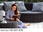 A woman is relaxing on the veranda of a country house and reading a book over a glass of red alcoholic drink or wine. The concept of relaxation and luxury wine. Стоковое фото, фотограф Photojuli / Фотобанк Лори