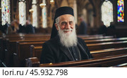 Smiling old christian priest inside church. Стоковое AI-видео, аниматор Александр Довянский / Фотобанк Лори