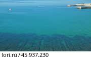 Panoramic view of the picturesque coastline with clear turquoise waters. A small boat can be seen in distance, and a concrete pier goes into the sea. The water is calm and clear, exposing seabed. Стоковое фото, фотограф Воловодов Владимир / Фотобанк Лори