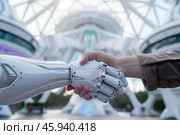 Close-up of a human hand shaking a robotic hand, symbolizing collaboration between humans and technology in a futuristic environment. Стоковое AI-изображение, AI-художник Михаил Строгалев / Фотобанк Лори
