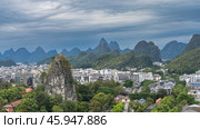Beautiful urban and mountain scenery. City buildings surrounded by green trees. A high cliff with steep slopes and a pavilion at the top. A mountain range against the sky and clouds. China. Guilin. Стоковое фото, фотограф Вера Ивановна Кубарева / Фотобанк Лори