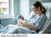 A woman in a hospital bed in the maternity ward. Mom has a newborn baby in her arms. Pregnancy and childbirth. Стоковое AI-изображение, AI-художник Photojuli / Фотобанк Лори