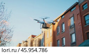 A flying drone delivers a parcel by air in a city with residential buildings in the background. Стоковое AI-видео, аниматор Александр Довянский / Фотобанк Лори