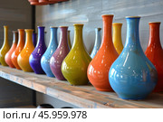 Colorful ceramic vases displayed on wooden shelf in modern home decor store. Стоковое AI-изображение, AI-художник Иван Рябоконь / Фотобанк Лори