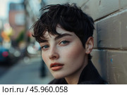 Young woman with pixie cut leaning against wall in urban setting. Стоковое AI-изображение, AI-художник Иван Рябоконь / Фотобанк Лори