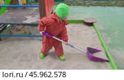 Child in orange snowsuit playing in sandbox with purple shovel. Outdoor playground scene. Winter clothing and activity concept. Стоковое видео, видеограф Андрей Журавлев / Фотобанк Лори