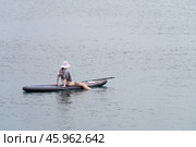 Russia, Bolshoi Utrish, September 16, 2024: a woman sits on a sapboard in a sea bay. Her feet are lowered into the water. Paddle and beach shoes on the board. Стоковое фото, фотограф Роман Дзюбало / Фотобанк Лори