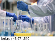 Close-up of scientists in lab coats performing an experiment using test tubes and beakers in a laboratory setting. Shallow depth of field. Стоковое AI-изображение, AI-художник Михаил Строгалев / Фотобанк Лори