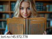 A young woman with long blonde hair and blue eyes, holding an old folder or book with notes in front of her. She is looking straight at the camera, her face is lit with soft light, emphasizing her natural beauty. The background consists of a blurred library with shelves filled with books, creating an atmosphere of knowledge, comfort and concentration. Стоковое AI-изображение, AI-художник Анна Кривицкая / Фотобанк Лори