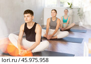 In sport studio with small group of friends, young man performs butterfly pose, Baddha Konasana. Стоковое фото, фотограф Яков Филимонов / Фотобанк Лори