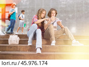 Girl prompts solution to problem to young man sitting on stone staircase in front of school. Стоковое фото, фотограф Яков Филимонов / Фотобанк Лори