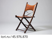 Elegant folding chair with brown leather seat and backrest on plain background. Стоковое AI-изображение, AI-художник Иван Рябоконь / Фотобанк Лори