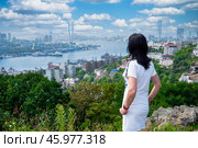 A 50-year-old Russian woman in a white dress stands in Nagorny Park, Vladivostok, admiring the view of Golden Horn Bay and the cityscape. Стоковое фото, фотограф Татьяна Терехина / Фотобанк Лори