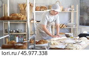Young male baker prepares raw yeast dough in bakery, shaping it into a baguette and rolls dough to give the shape of future bread. Стоковое видео, видеограф Яков Филимонов / Фотобанк Лори