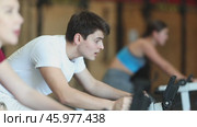 Man on an exercise bike during a group workout to the gym. European in a tracksuit visits a fitness club and works out on a cardio machine. Стоковое видео, видеограф Яков Филимонов / Фотобанк Лори