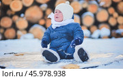 Tearful infant bundled in winter attire sobbing on snow covered wooden logs during wintry weather. Стоковое фото, фотограф Mikhail Davidovich / Фотобанк Лори