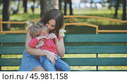 Caring mother gently comforting sobbing child on wooden park bench, offering emotional support and warmth. Стоковое фото, фотограф Mikhail Davidovich / Фотобанк Лори