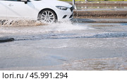 White car making splashes driving through flooded street after heavy rain, creating large puddles and water splashes. Стоковое фото, фотограф Mikhail Davidovich / Фотобанк Лори