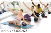Multinational athletes sitting on floor in asana pigeon do body tilts to side, use fitball. Стоковое видео, видеограф Яков Филимонов / Фотобанк Лори