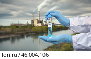PFAS тест проверка качества и загрязнения воды. В руках лаборанта тест пробирка с водой из реки. Напротив дымящий завод. Стоковое AI-изображение, AI-художник Денис Костров / Фотобанк Лори