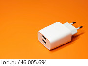 Белый блок питания с двумя портами USB без кабеля на оранжевом фоне. Адаптер питания, зарядное устройство для бытовой электроники. Редакционное фото, фотограф Sergei Gorin / Фотобанк Лори
